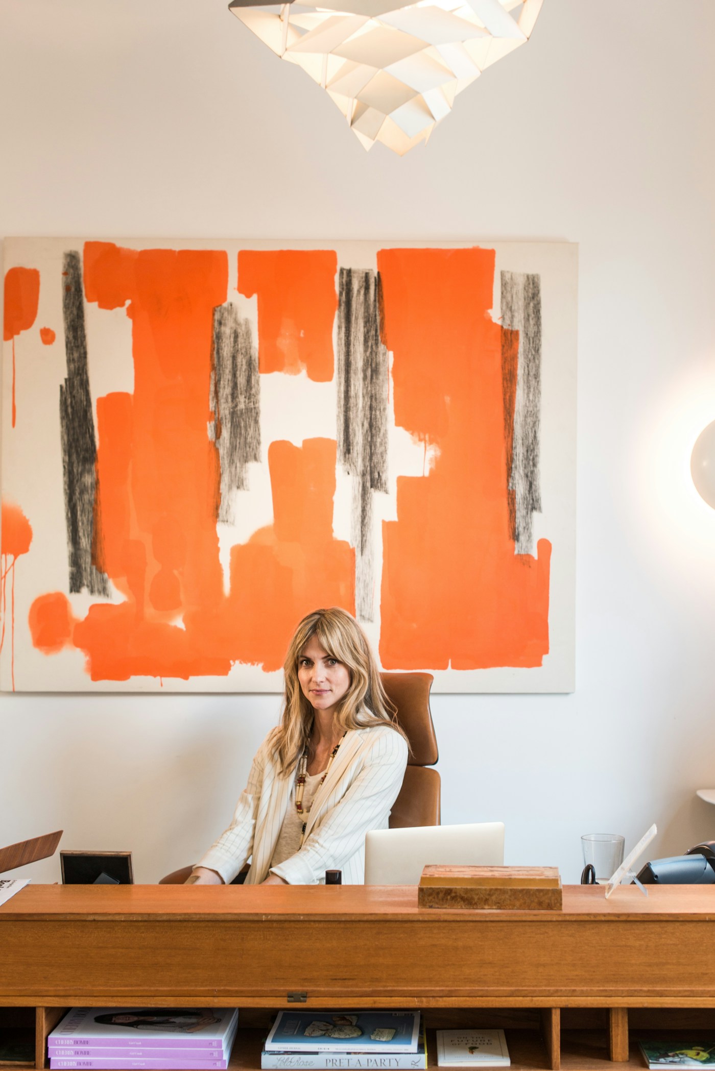 Becca Parrish seated behind a wooden desk beneath a large orange abstract painting