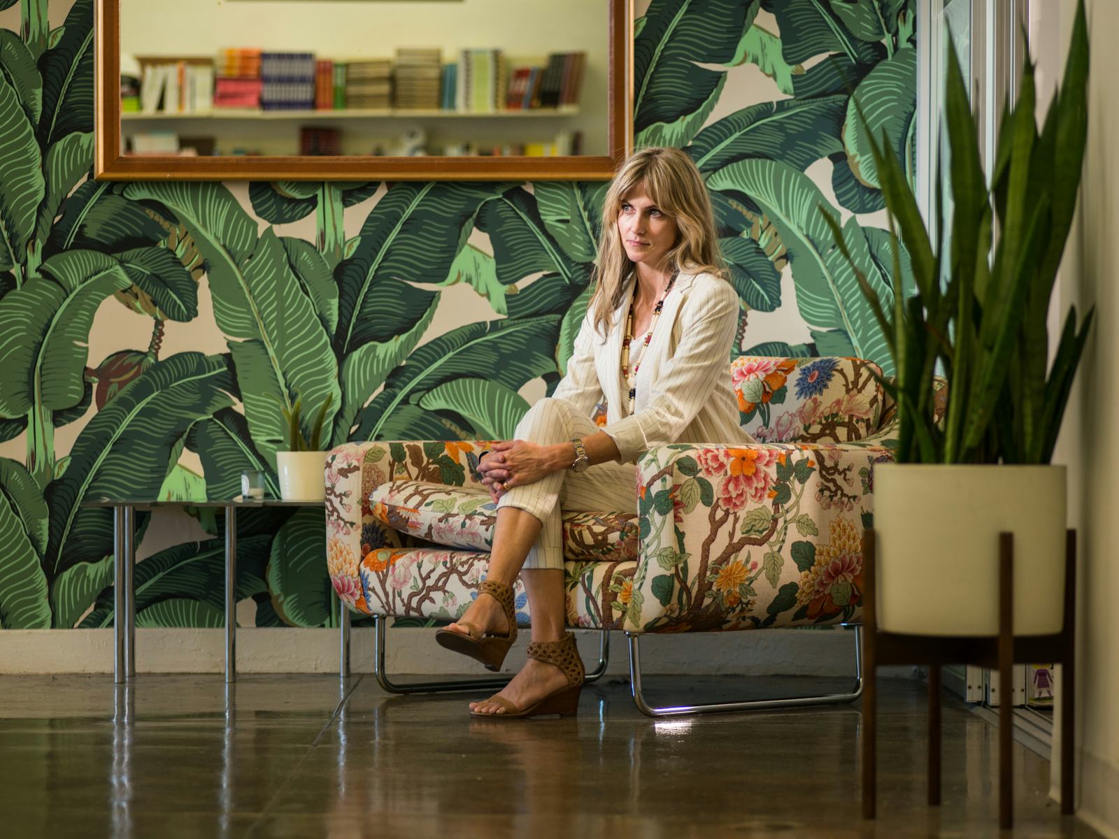 Becca Parrish seated in a patterned chair against a leafy wall