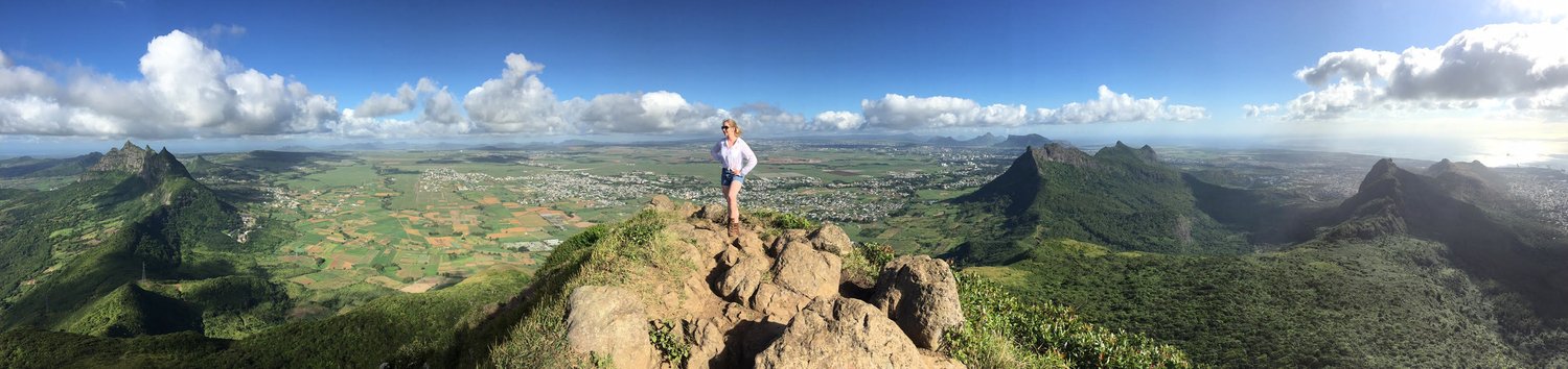 Beck Bamberger standing on a mountain ridge in Mauritius above a wide green valley