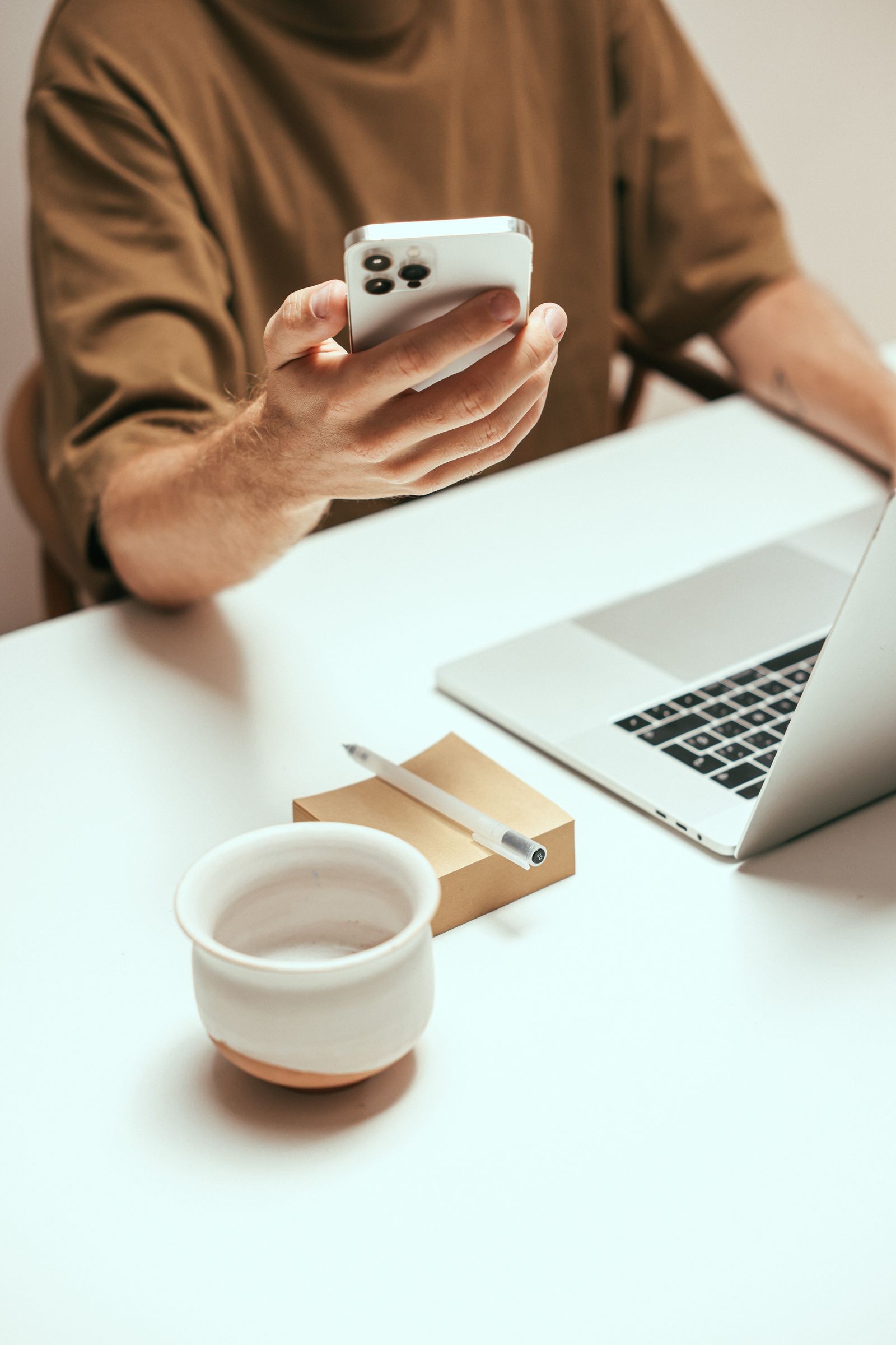 A person using a phone at a desk with a laptop