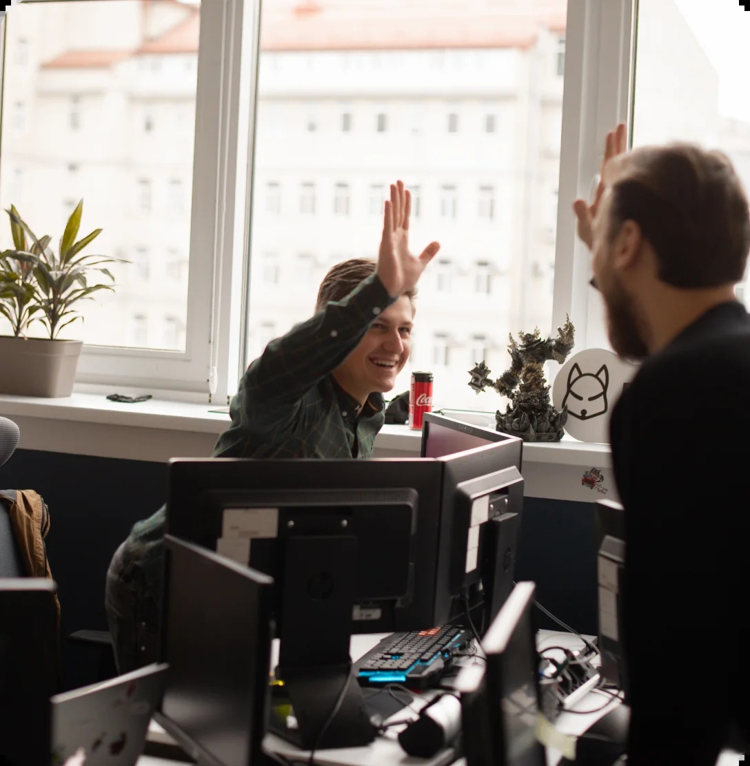 Two Belkins colleagues raising their hands for a high-five across office monitors