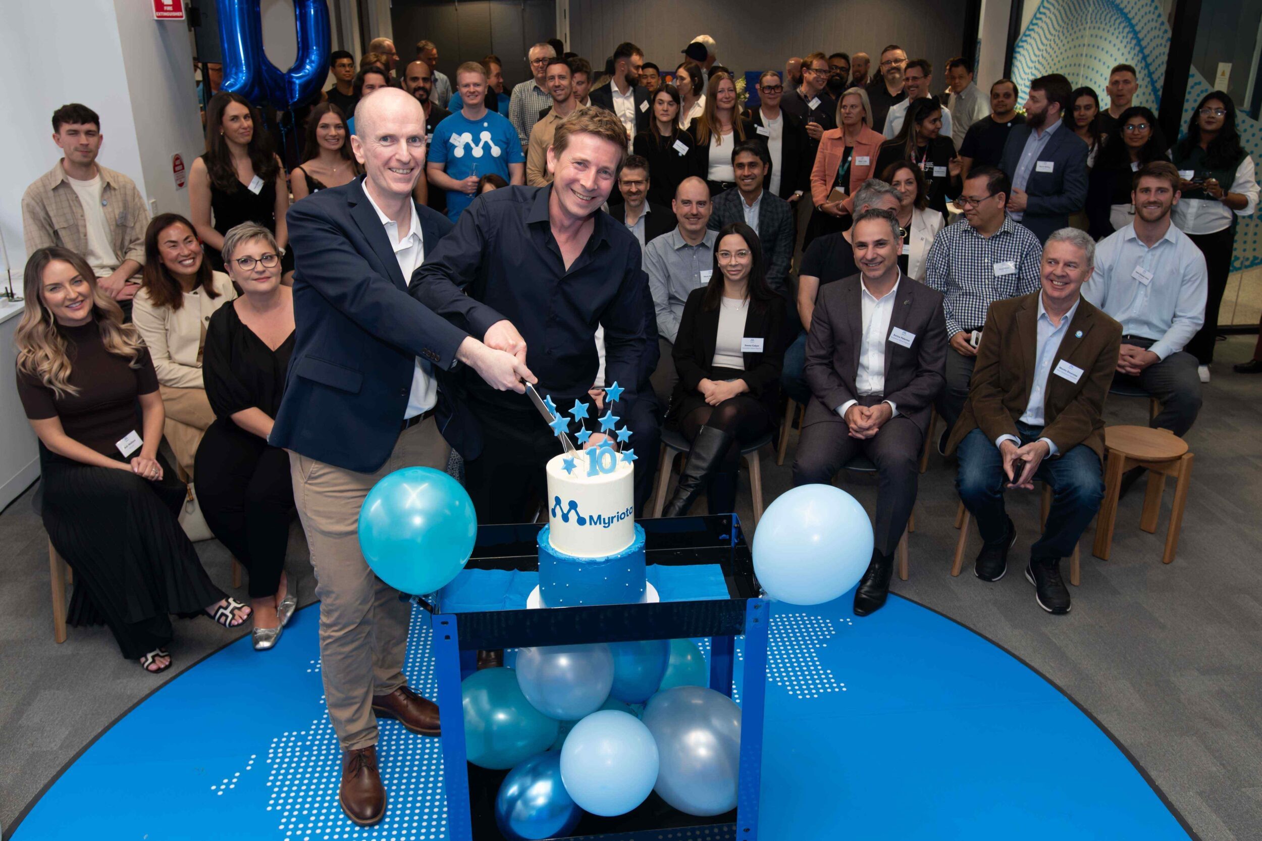 David Haley, left, and Ben Cade cutting Myriota’s tenth-birthday cake with colleagues gathered around them