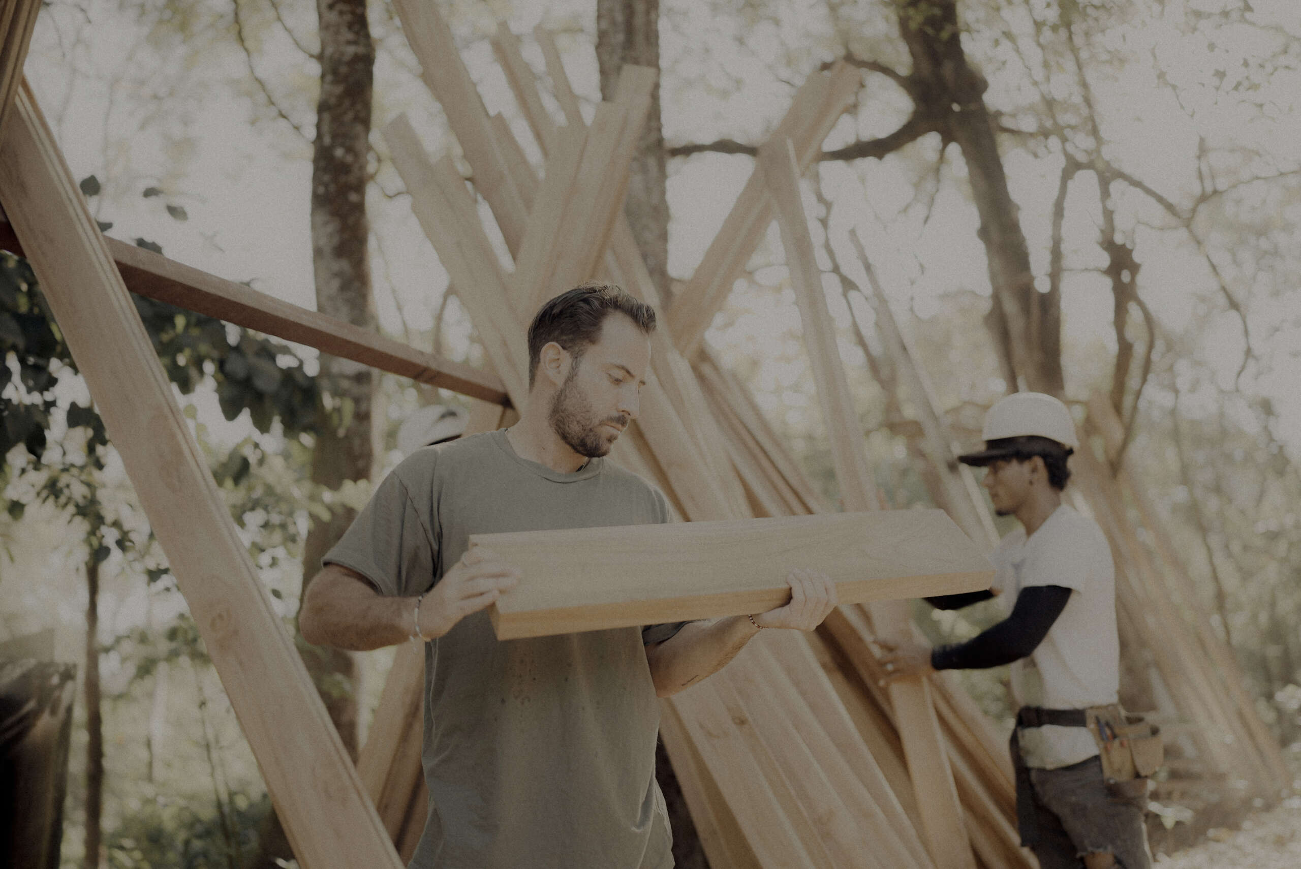 Ben Lee carrying timber at the re:center construction site, with another worker behind him.