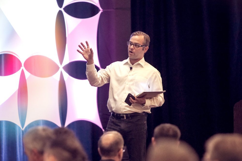 Ben Powers speaking to an audience while holding a tablet