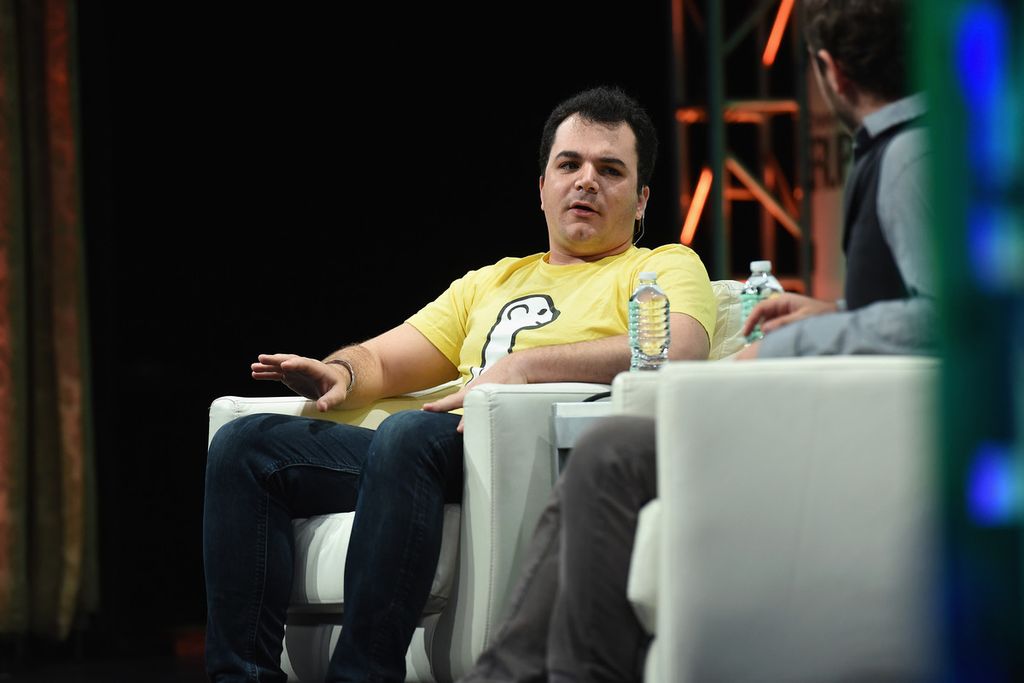 Ben Rubin speaking onstage in a yellow Meerkat shirt during a technology conference panel