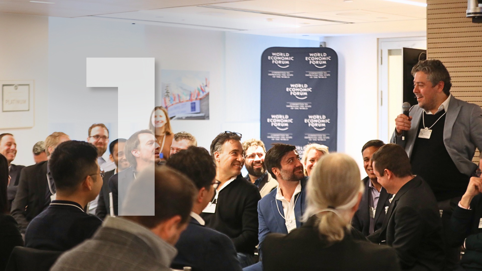 Benj Conway standing with a microphone while speaking to a seated group at a World Economic Forum gathering