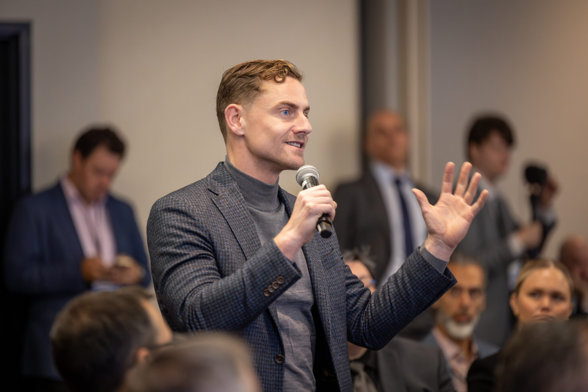 Benjamin Bergen holding a microphone and addressing a seated audience at a CCI gathering