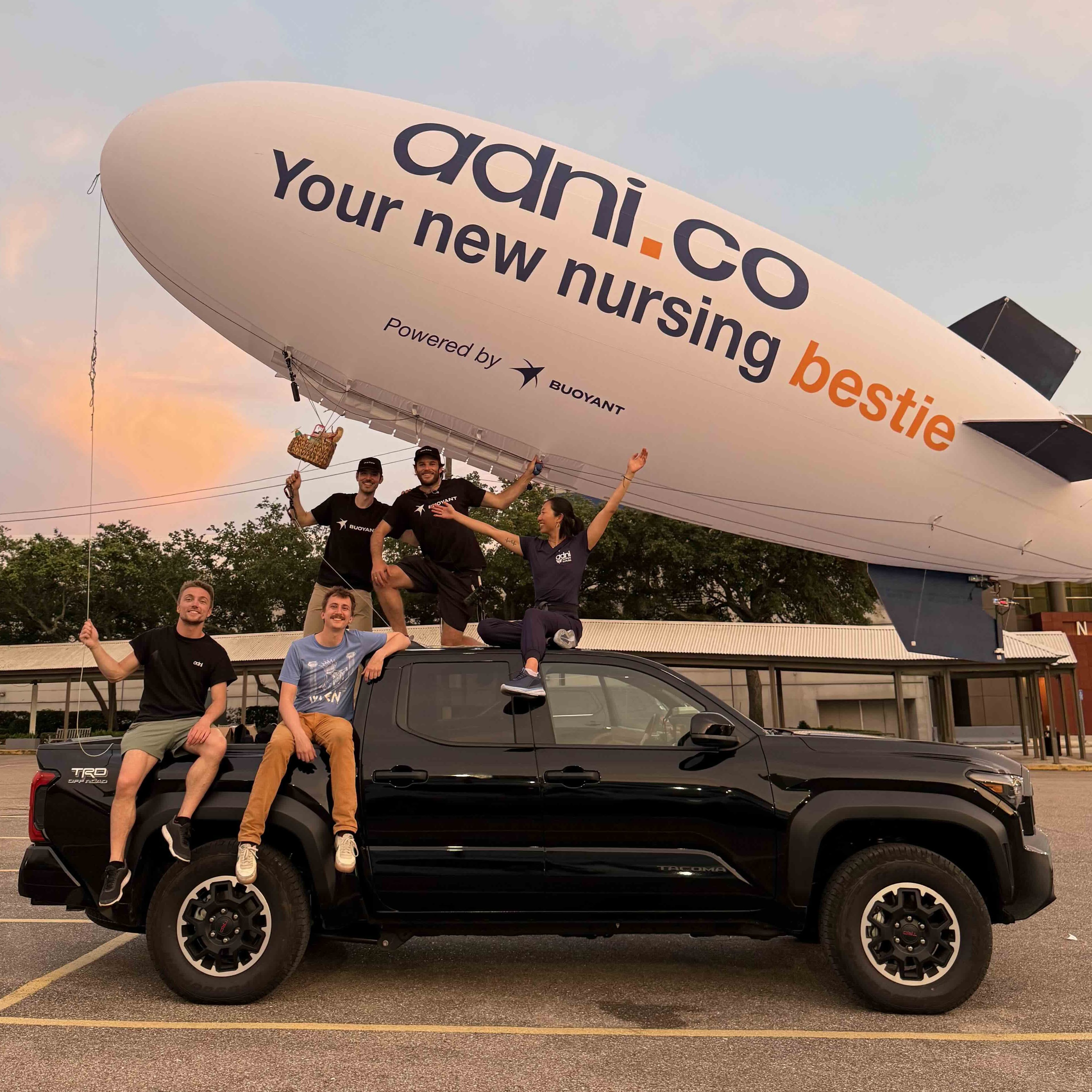 The Buoyant Aero team poses with an Adni-branded blimp above a pickup truck