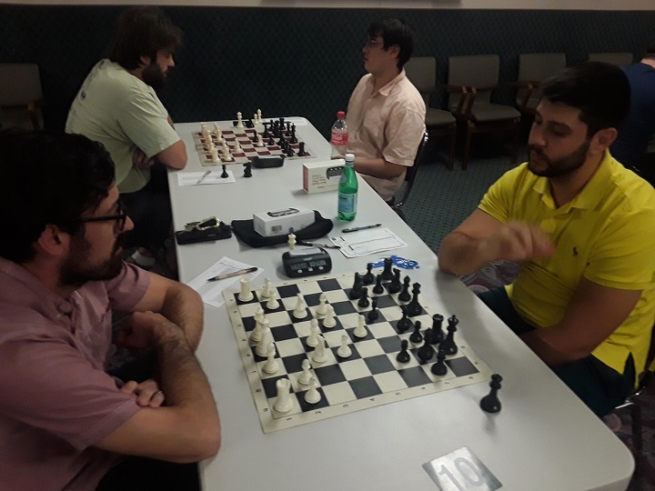 Benji Twerskoi, in yellow, studies a chess position across from Adam Huber at Denver Chess Club