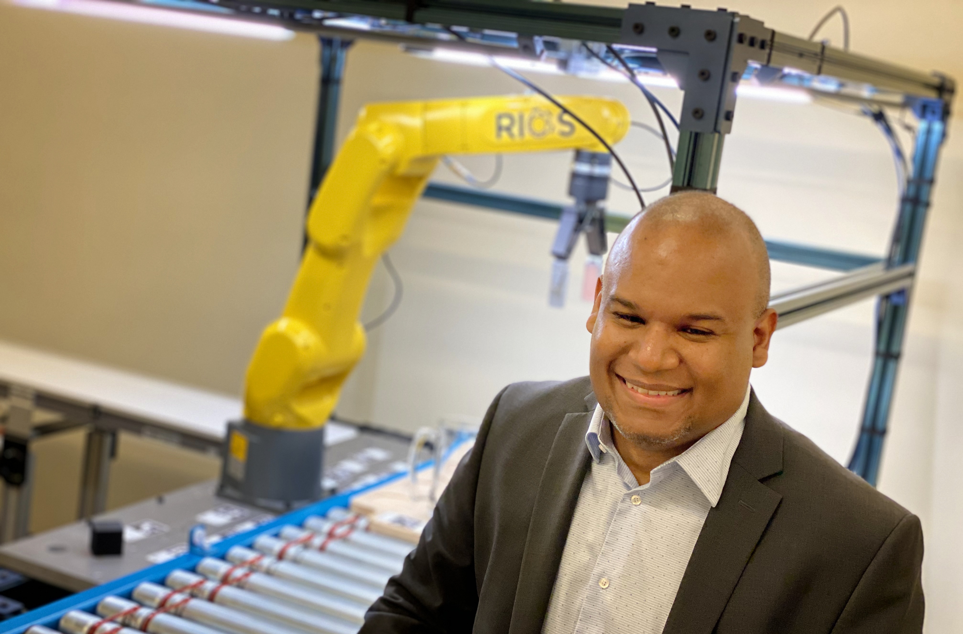 Bernard Casse beside a yellow RIOS industrial robot and a conveyor