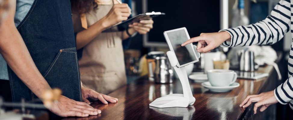 A customer reaches toward a tablet on a café counter