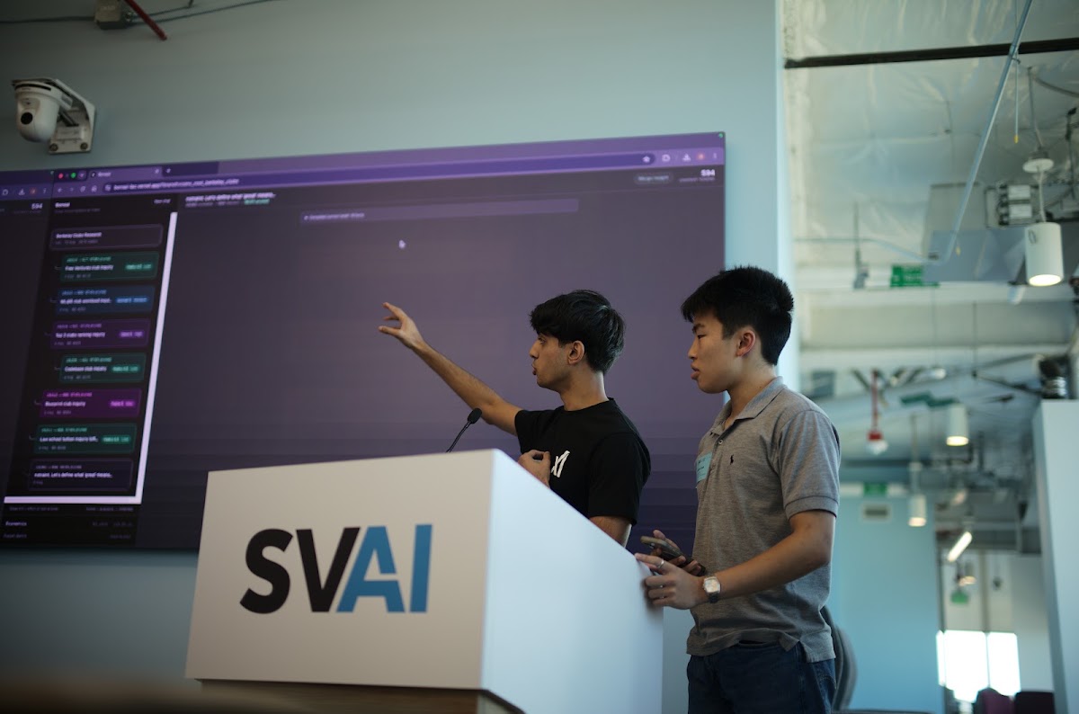 Two hackathon participants presenting their project beside a large code display