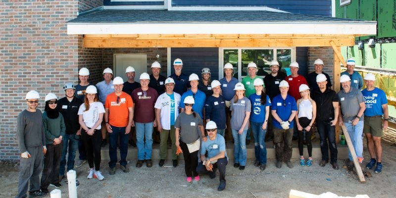 Executive Build volunteers, including Beth McDonald, standing outside a house under construction