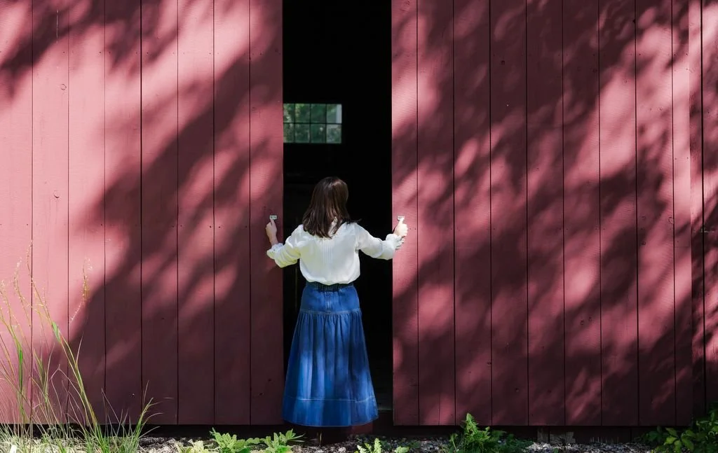 Beth Monaghan, seen from behind, opening red wooden barn doors