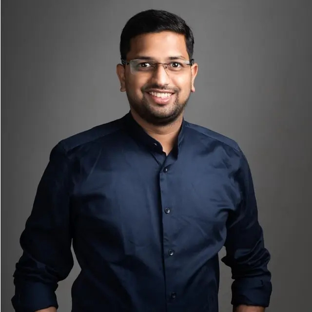 Bhushan Muthiyan in a dark blue shirt against a gray studio background