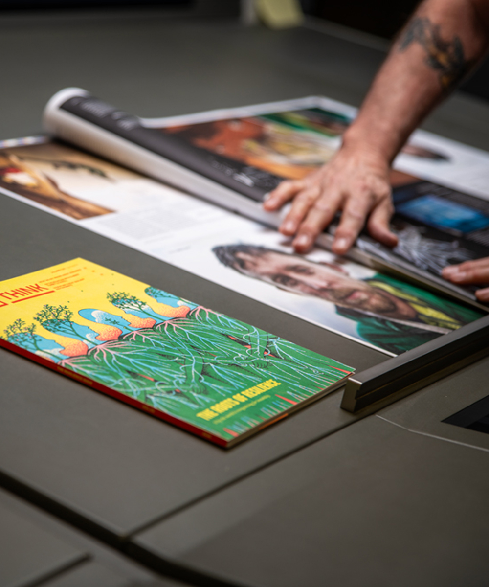 A reader turns the pages of a Big Think magazine beside The Roots of Resilience issue