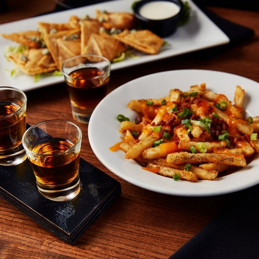 Whiskey tasting glasses beside loaded fries and appetizers at Big Whiskey’s