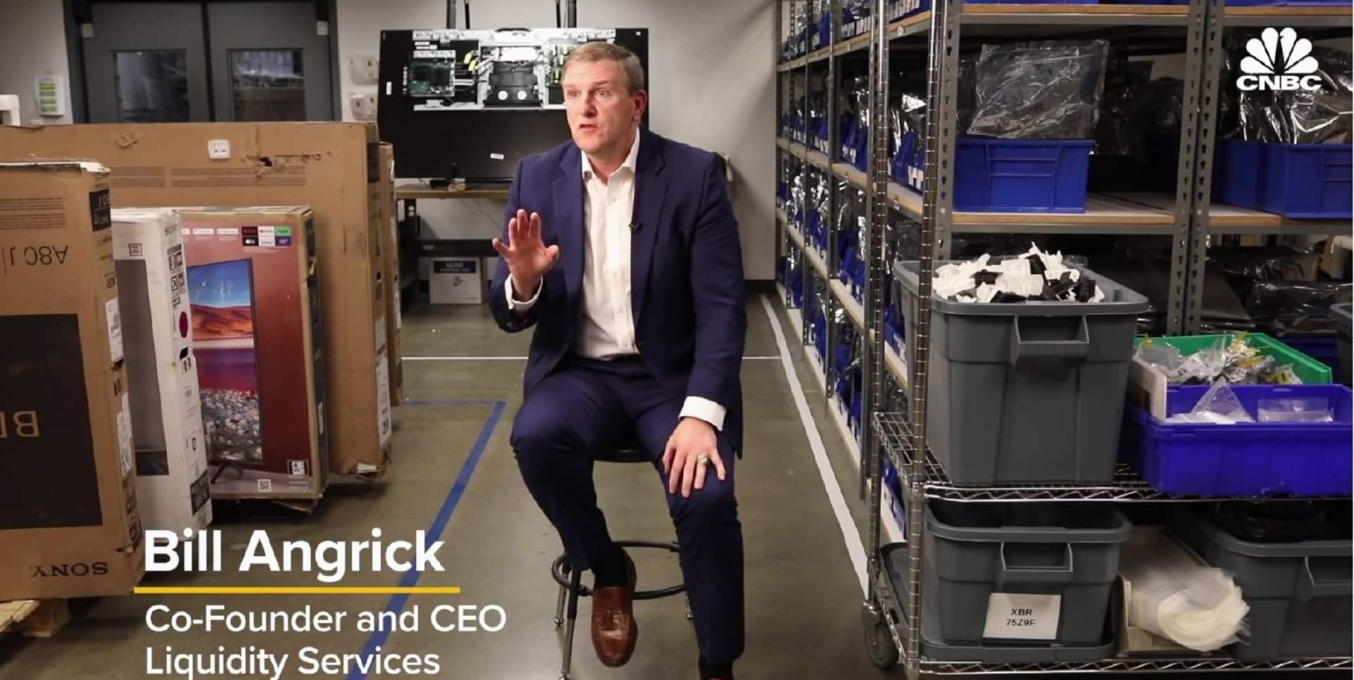 Bill Angrick seated among boxed televisions and warehouse shelving during a CNBC interview