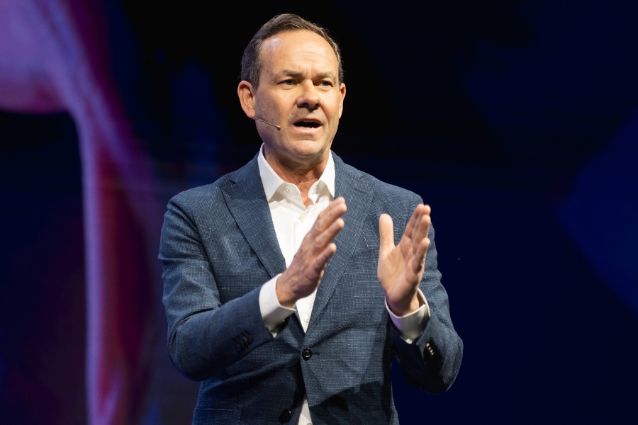 Bill Crager speaking onstage, wearing a headset microphone and gesturing with both hands