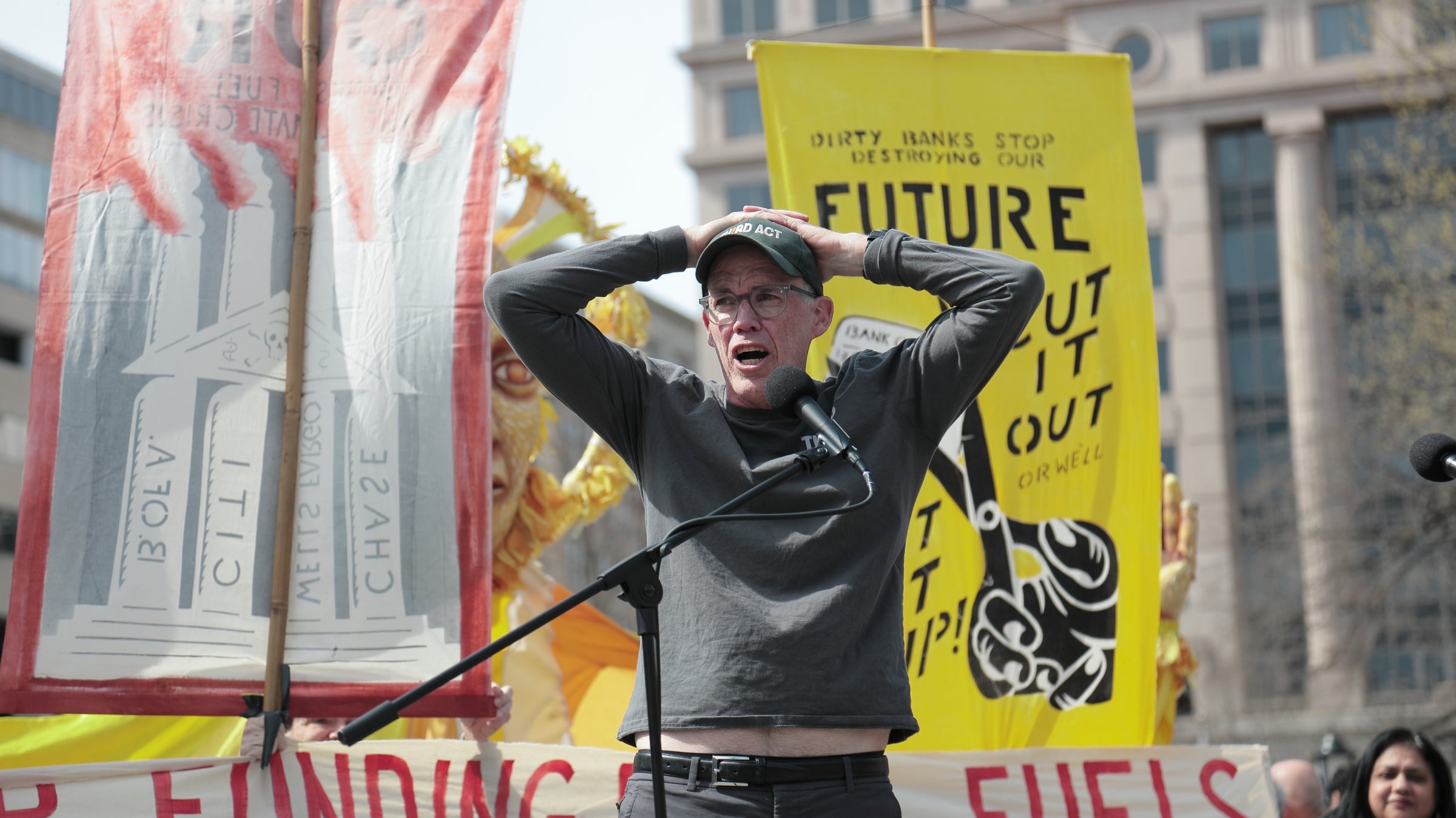 Bill McKibben speaking at a Third Act climate demonstration in Washington, D.C., with bright protest signs behind him