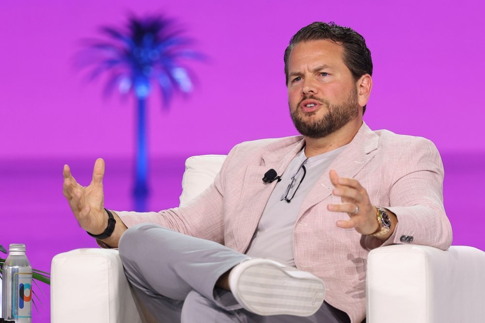 Bill Ready seated on a stage in a pale pink jacket, gesturing during a conversation