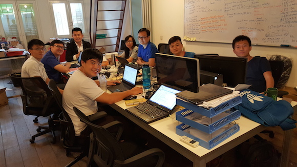 Taidii colleagues around office desks; Wang Bin is seated at the back wearing a jacket.