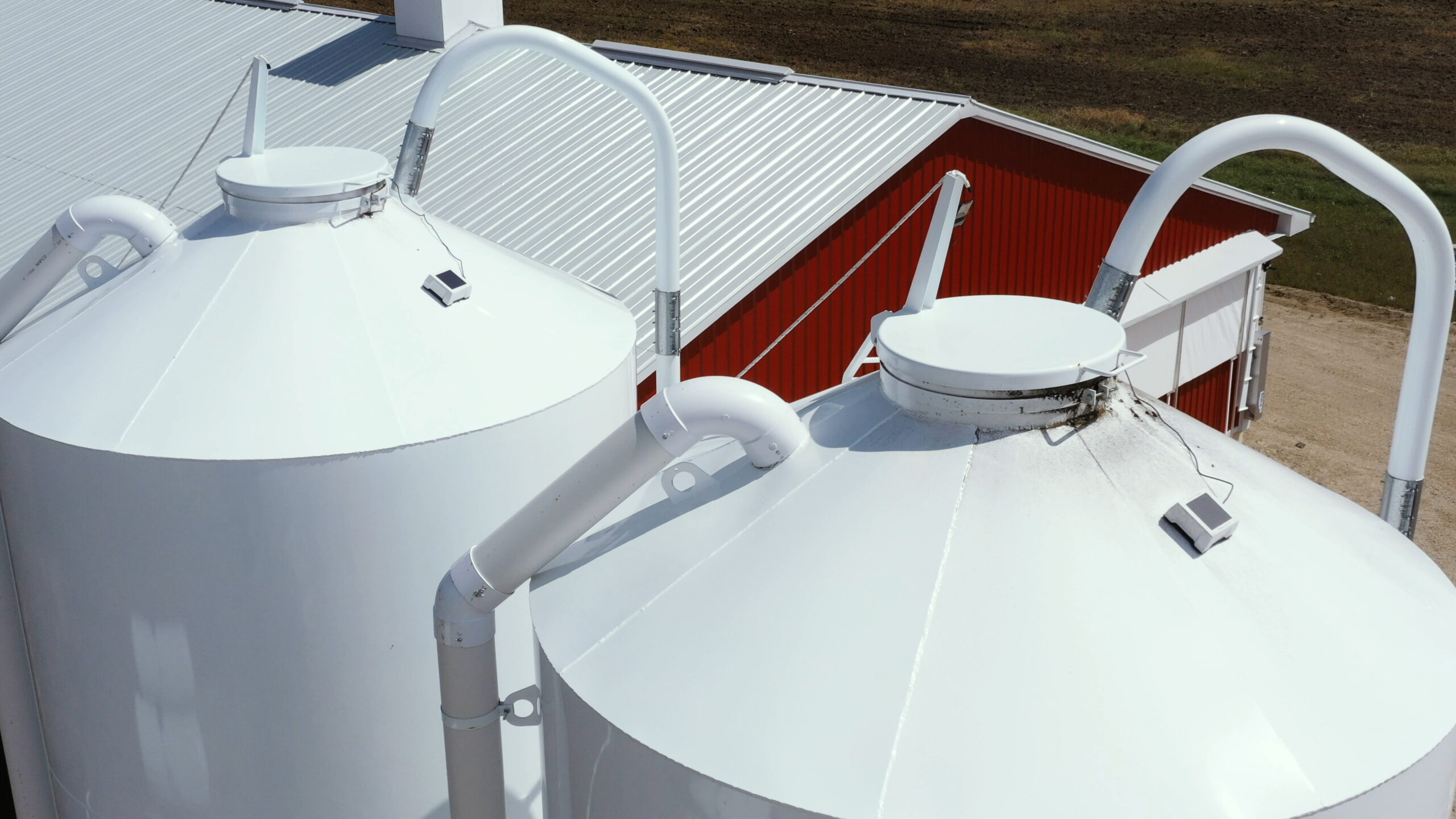 BinSentry sensors installed on white outdoor feed bins beside a red barn