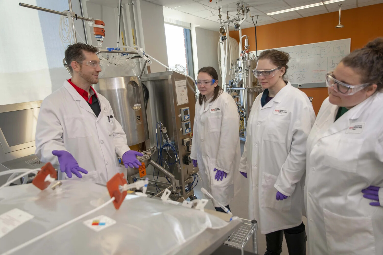 Scientists in lab coats gather around industrial bioprocessing equipment