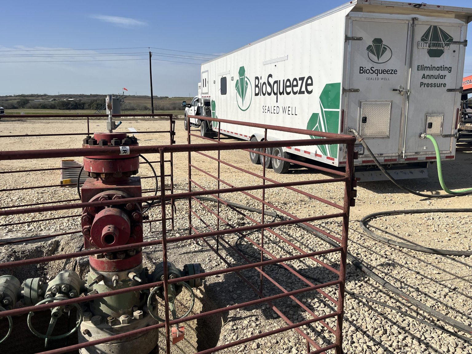A BioSqueeze 'Sealed Well' mobile treatment unit parked at an oil and gas wellsite, with a wellhead in the foreground.