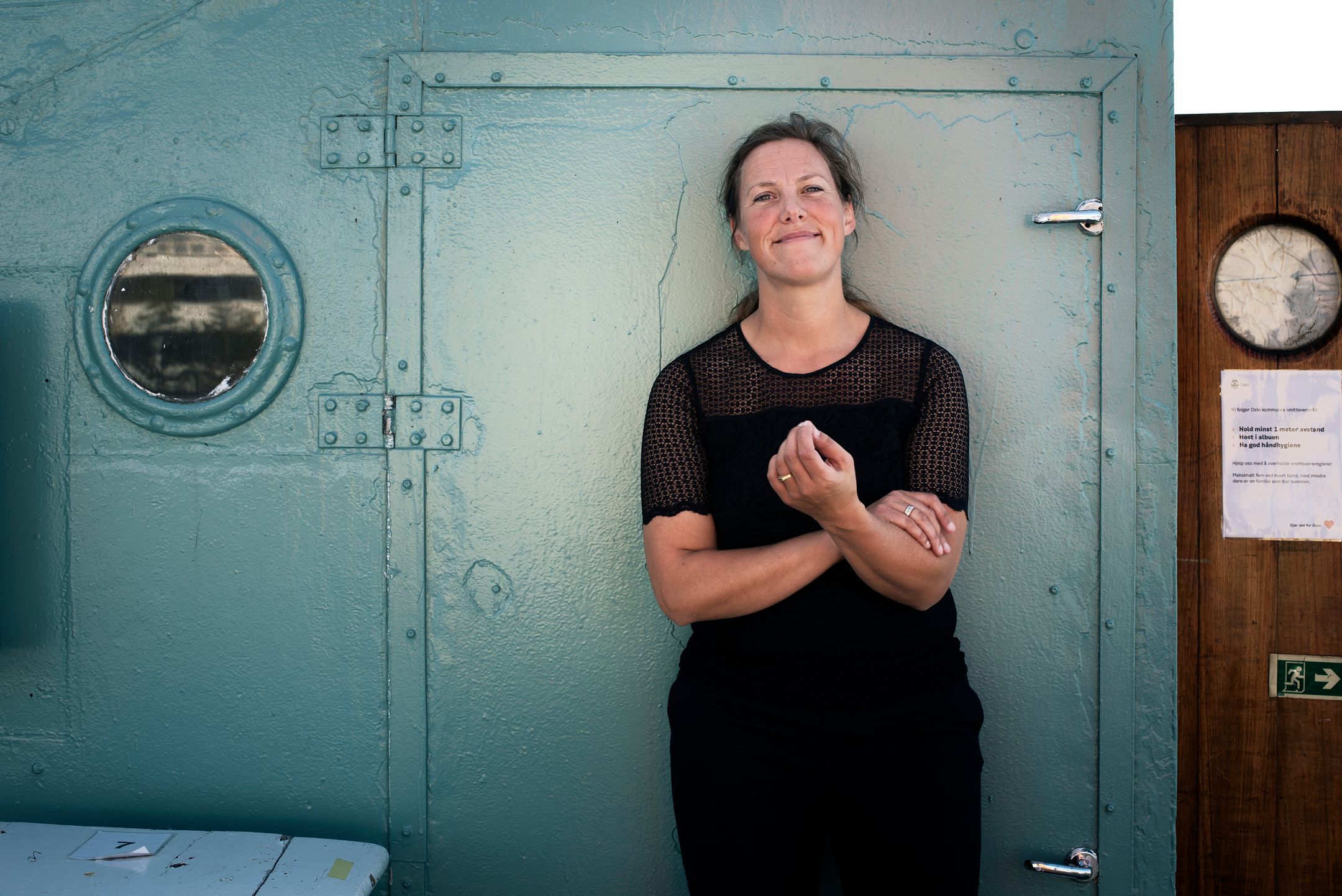 Birgit Liodden standing beside a blue-green ferry door and porthole in Oslo