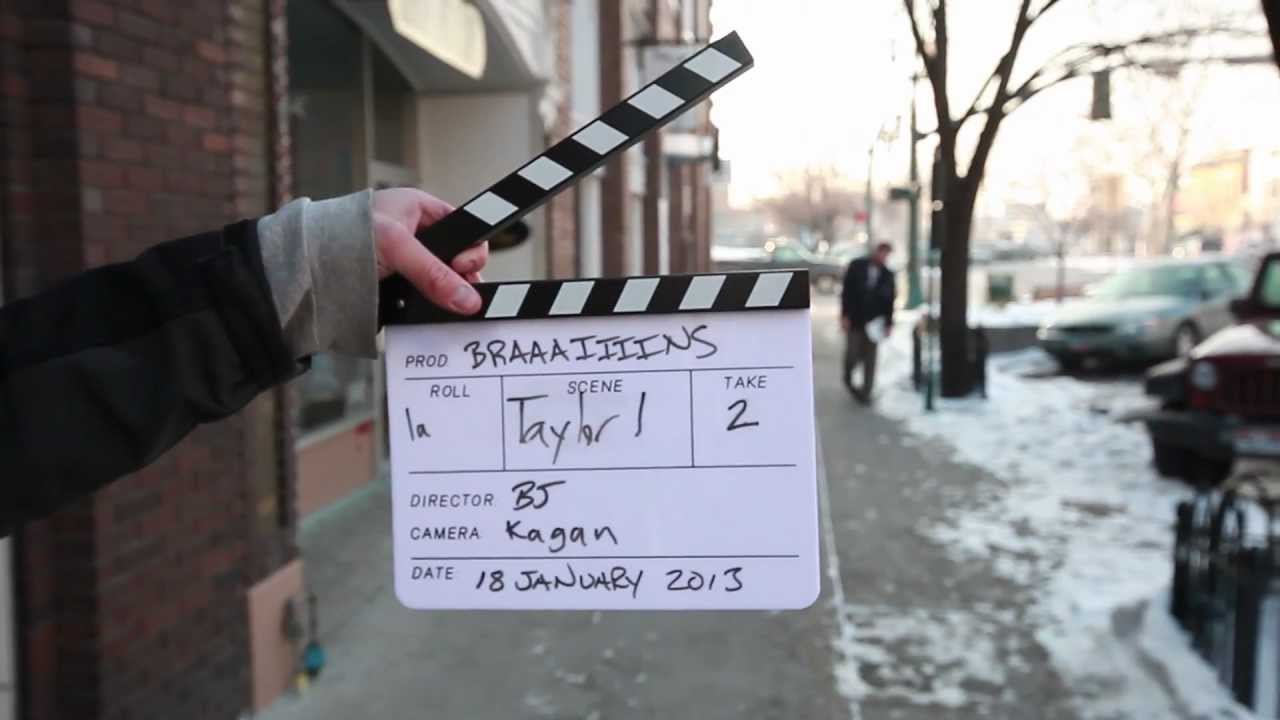 A film clapperboard labeled BRAAIIIINS, with BJ listed as director, held on a snowy street