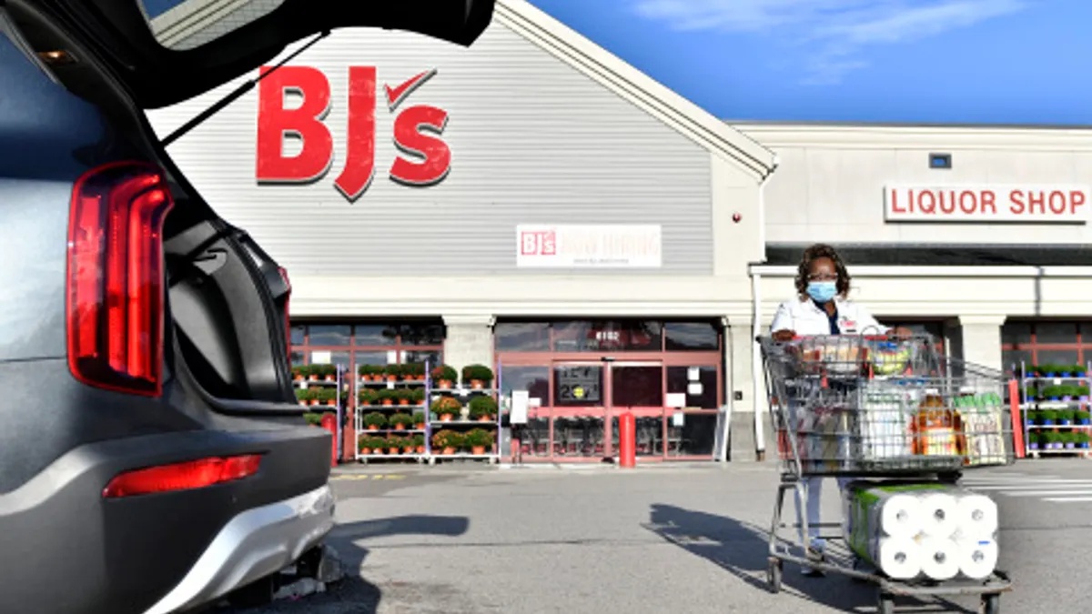 BJ’s employee wheels a grocery order toward an open vehicle outside a club