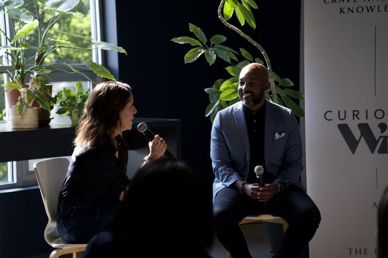 Blair Brady, holding a microphone, in conversation with TJ Abrams at Curious WITH