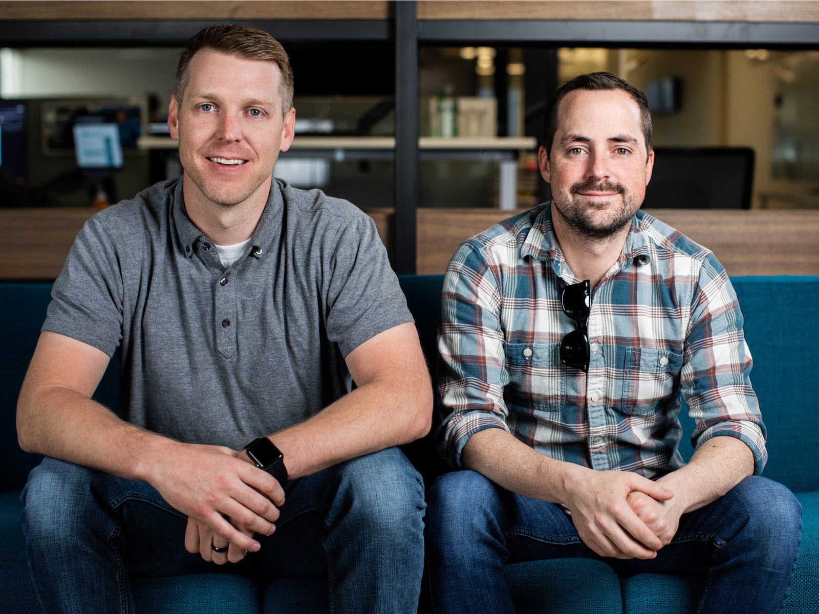 Divvy co-founders Alex Bean, left, and Blake Murray, right, seated together on a blue office sofa.