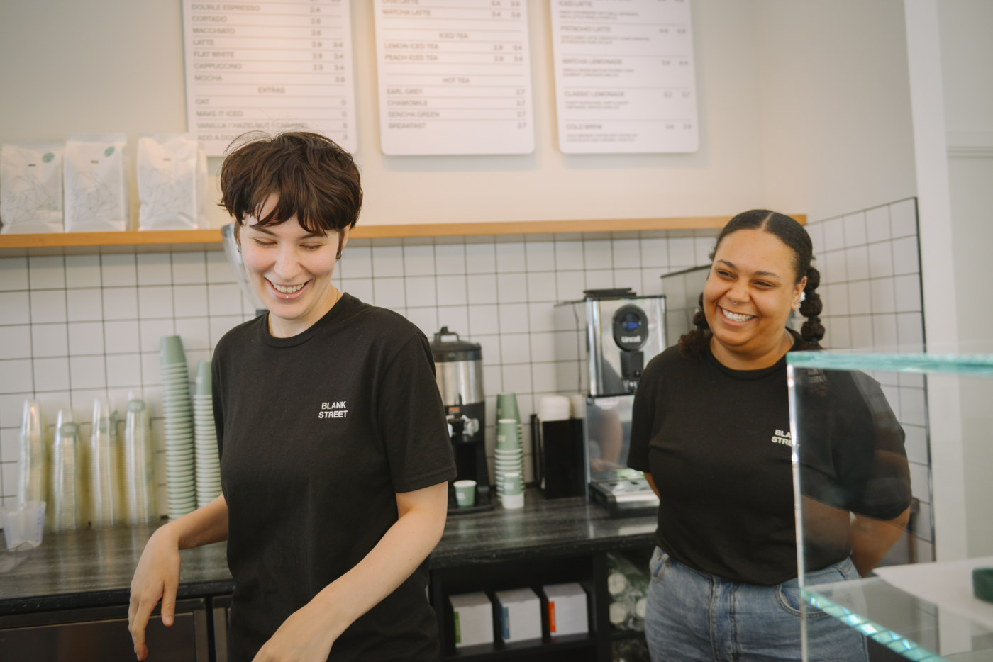 Two Blank Street baristas smiling behind the counter in a cafe