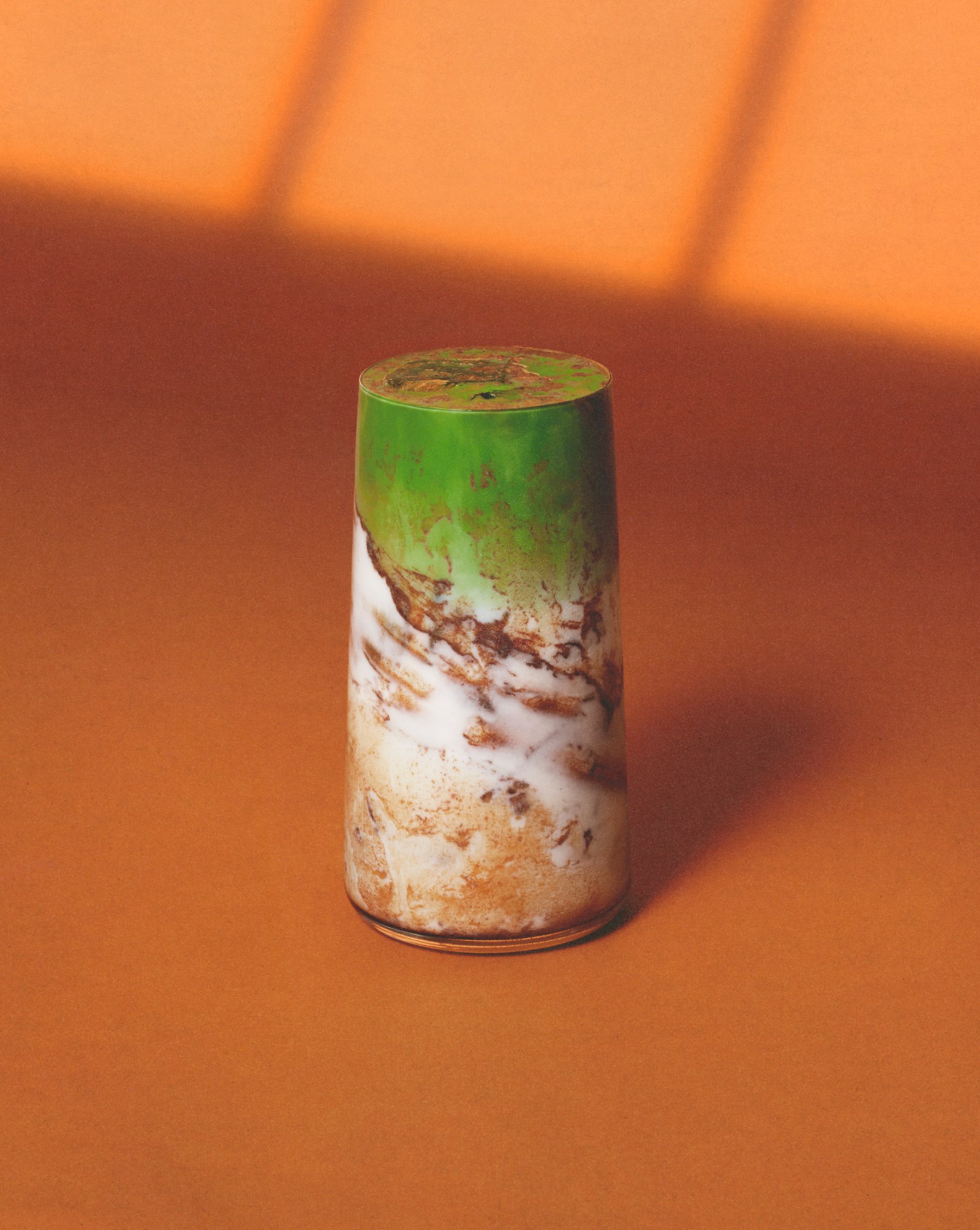 A cinnamon bun matcha drink photographed against a warm orange background