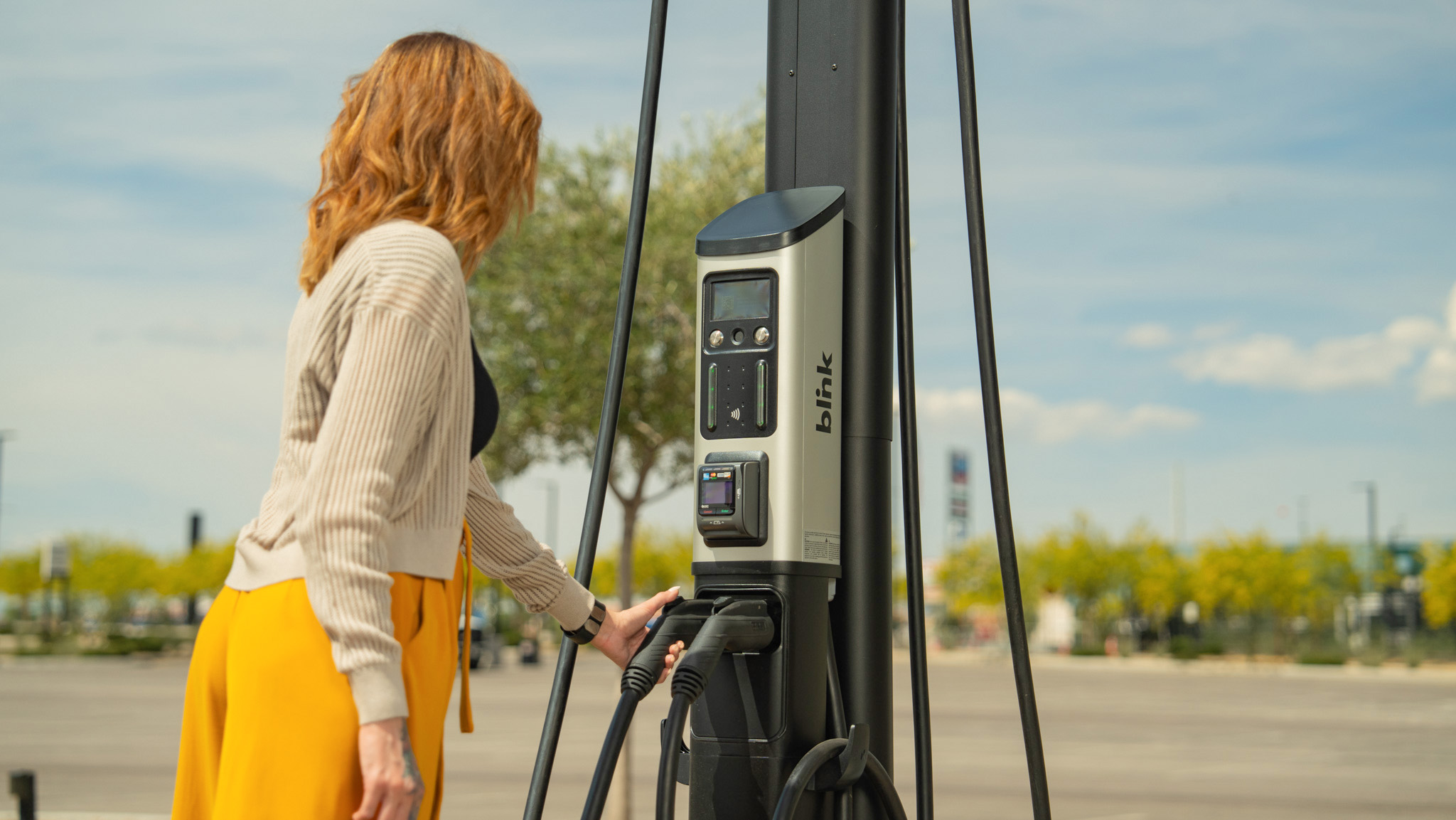 A driver reaches toward a Blink charging station in an outdoor parking area