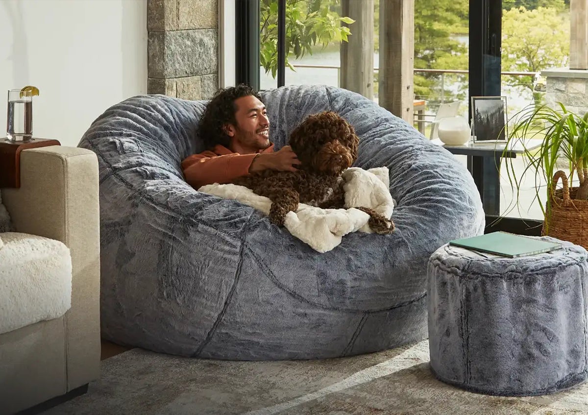 A person and a dog relaxing on a large gray Lovesac chair in a bright living room