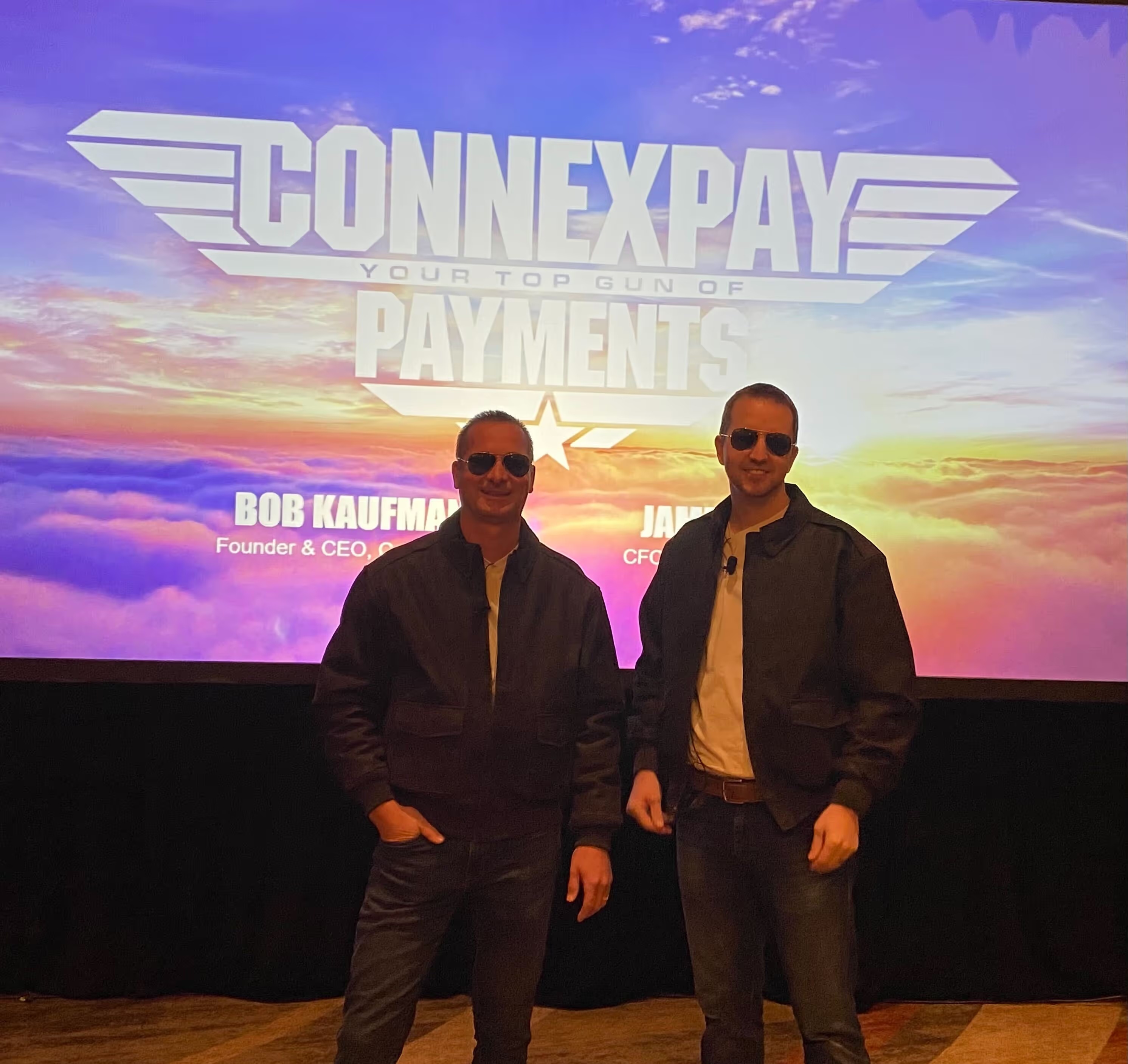 Bob Kaufman, left, and James Hall wearing aviator sunglasses in front of a ConnexPay Top Gun-themed presentation