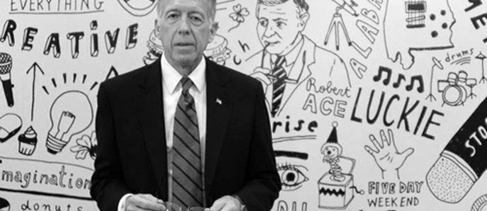 Bobby Luckie in a suit standing before an illustrated wall filled with creative motifs