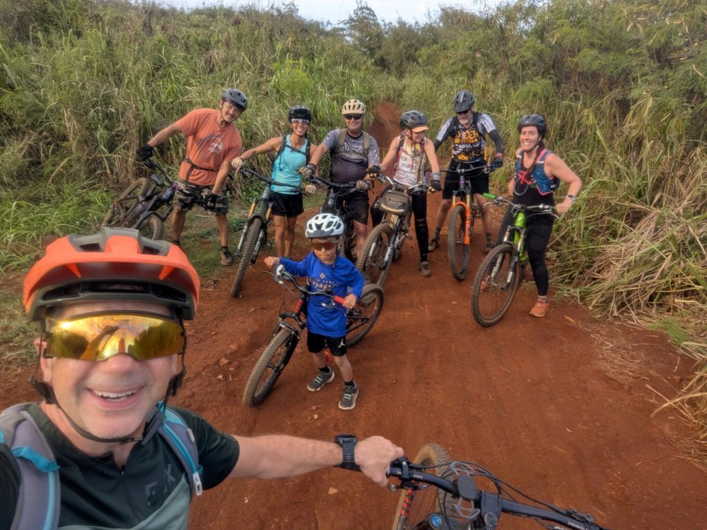 A group of MTB Kauai riders with their bikes on a red dirt trail