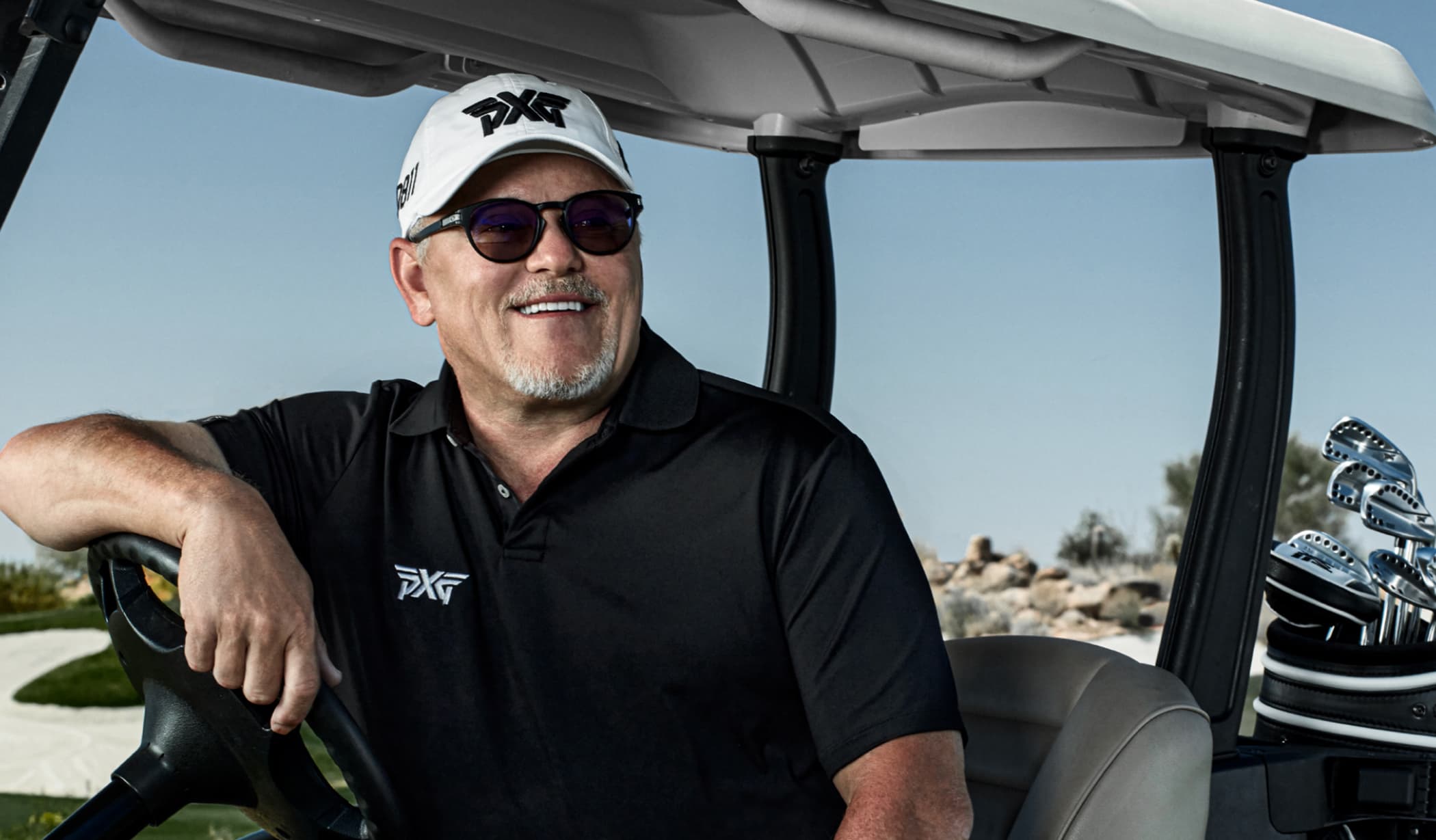 Bob Parsons smiling in a golf cart, with a set of PXG irons beside him
