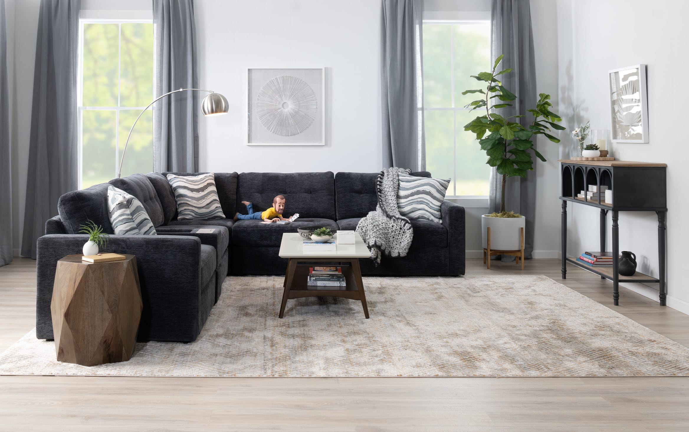 Charcoal modular sectional in a furnished room, with the Little Bob character stretched across a cushion