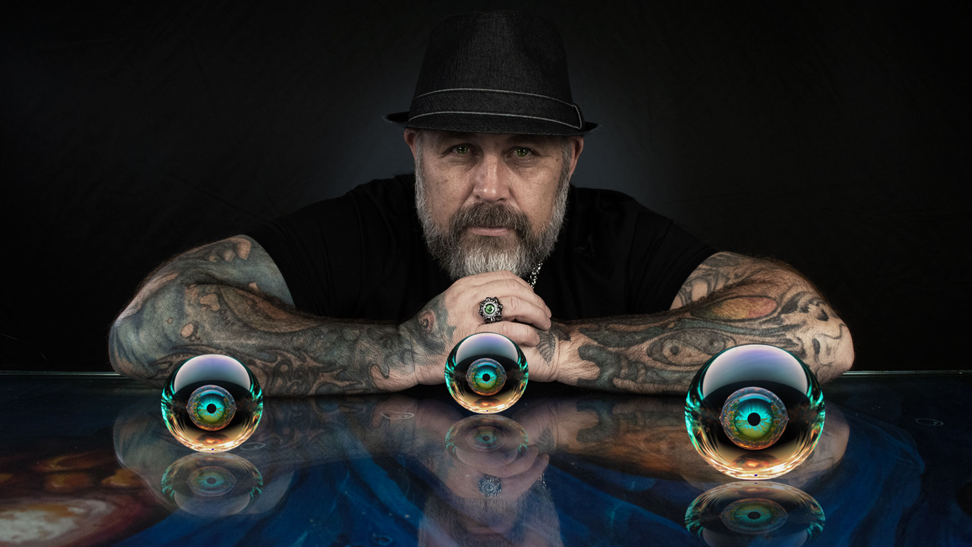 Peter Bogdanov in a black hat, seated behind three reflective glass spheres