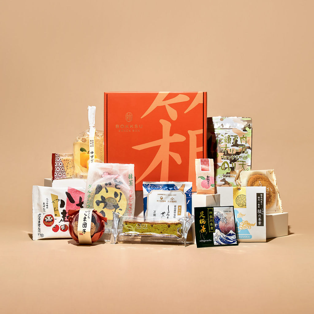 An open orange Bokksu box surrounded by colorful Japanese snacks