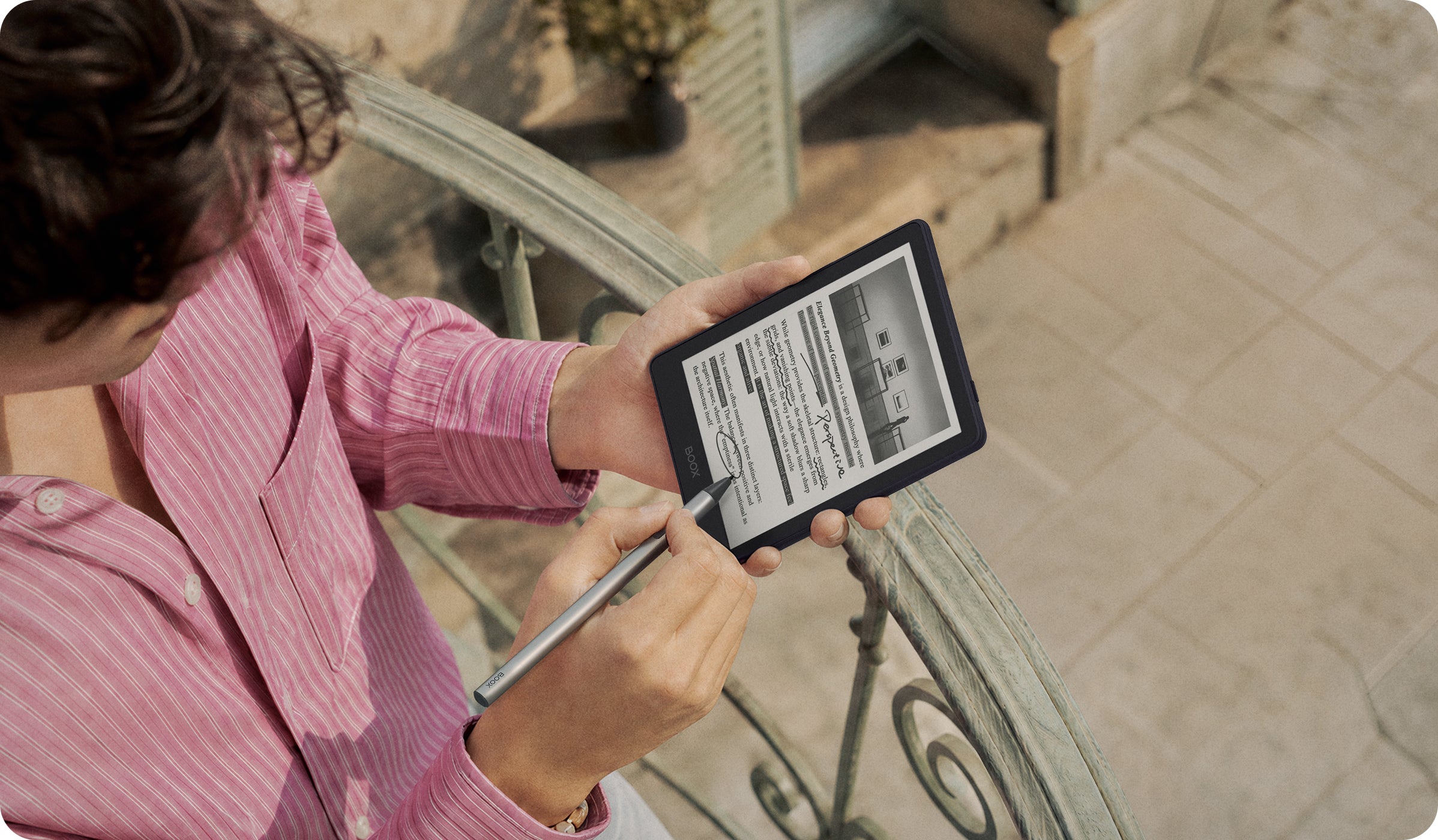 A person in a striped pink shirt writing on the BOOX Go 6 Gen II with a stylus outdoors