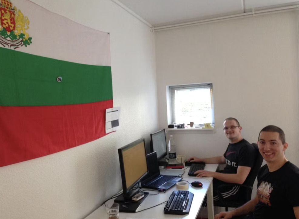 Boris Krastev and Boris Borisov seated at desks in RemoteMore's first office beneath a Bulgarian flag
