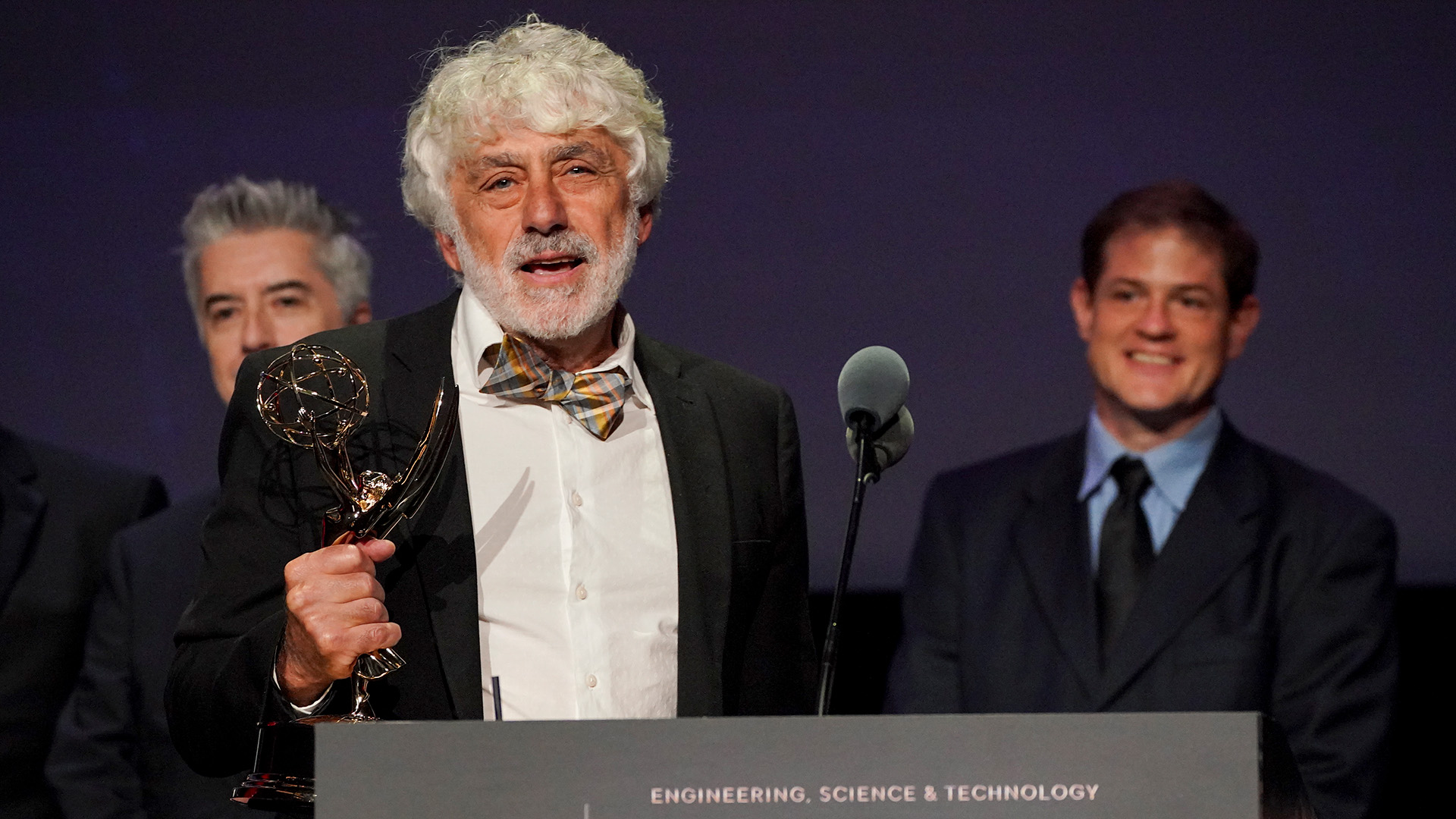 Boris Yamnitsky holding an Emmy at the microphone with colleagues behind him