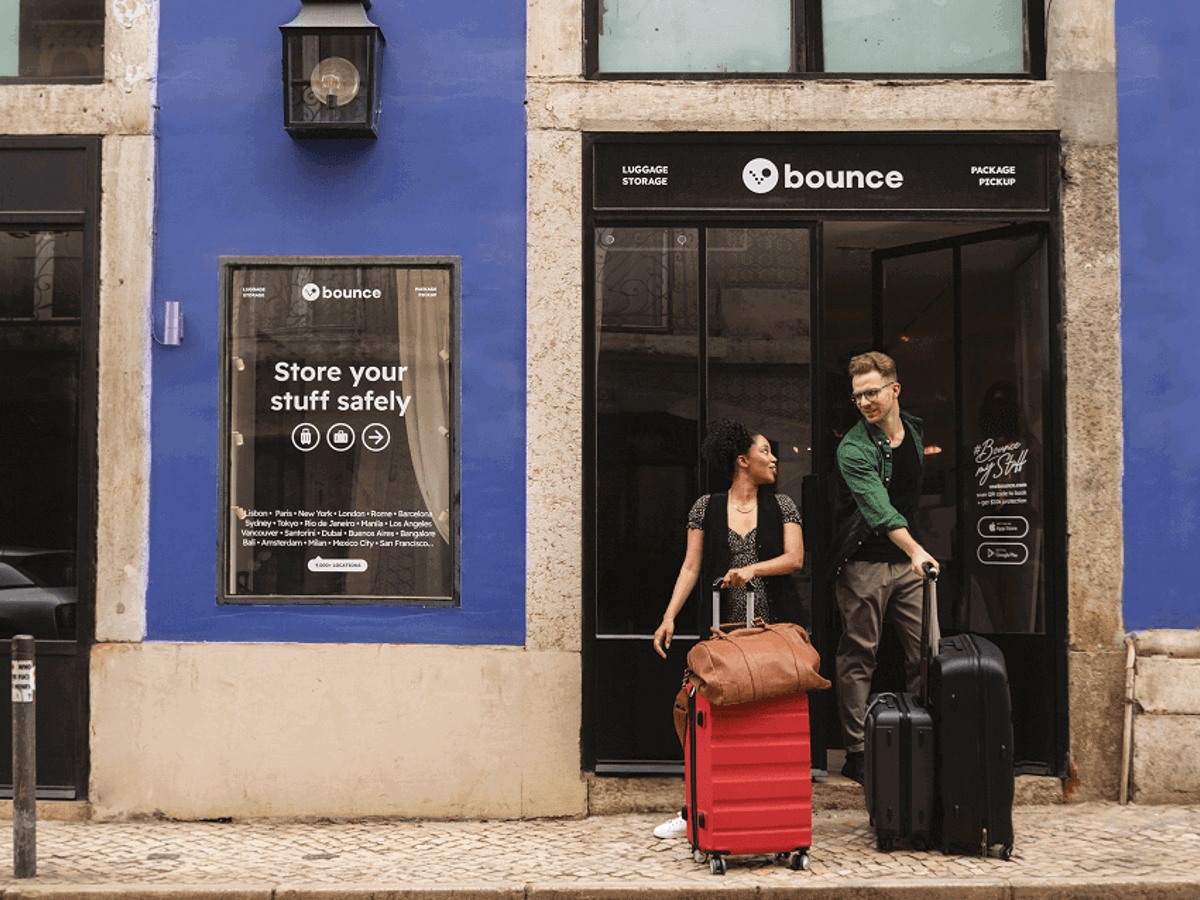 Travelers with rolling bags outside a Bounce-branded storage storefront