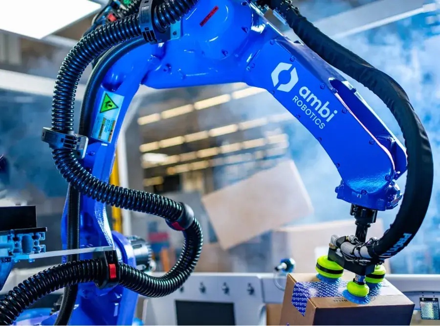 Blue Ambi Robotics arm lifting a cardboard parcel with suction grippers